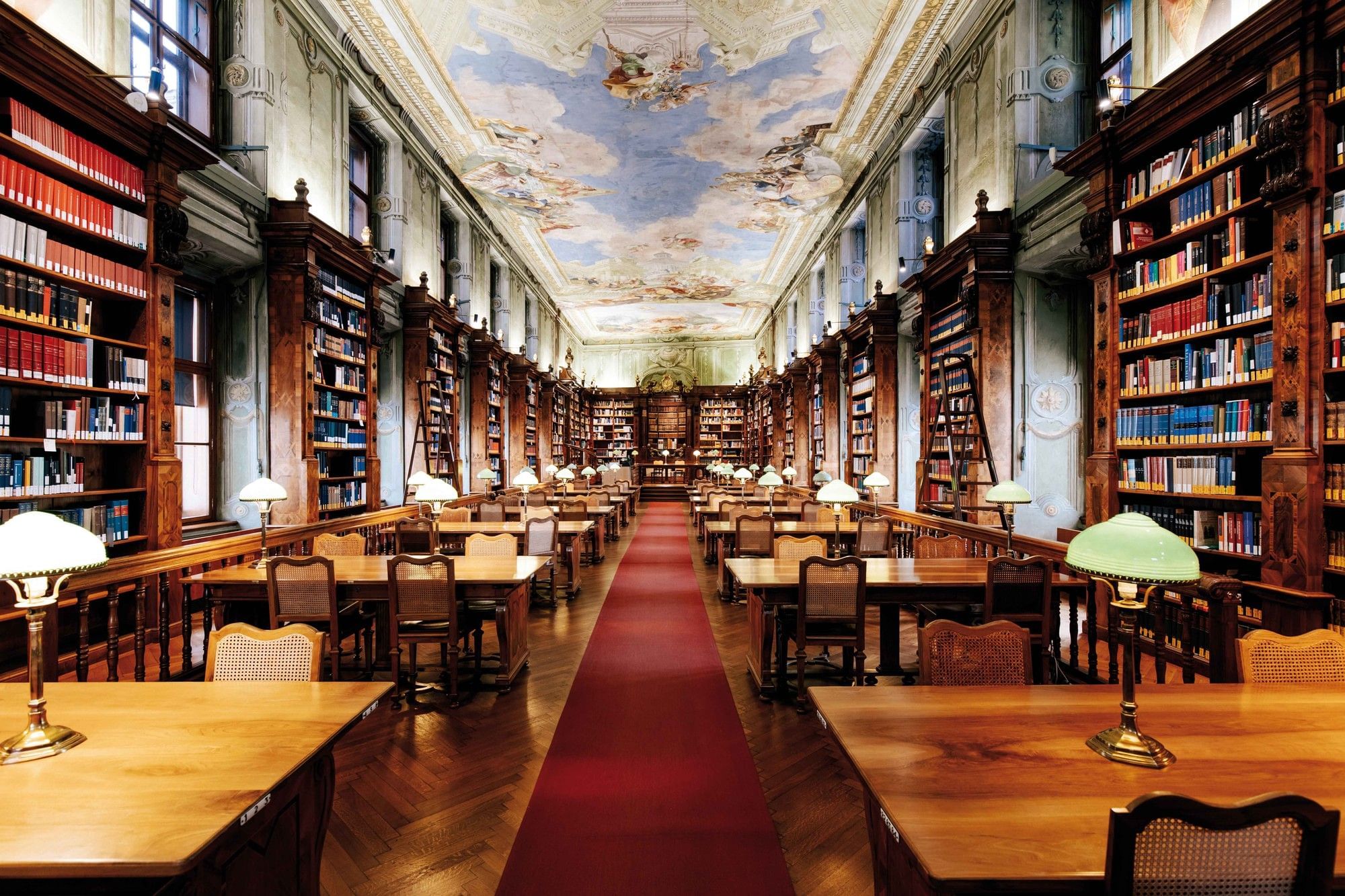 Historic reading room of the Austrian National Library in Vienna with bookshelves, ceiling fresco and classic reading lamps