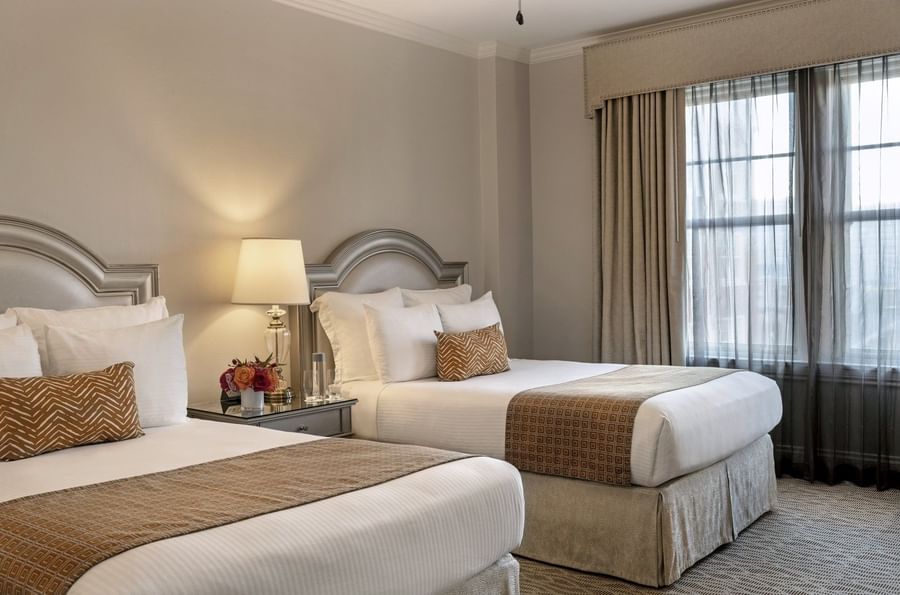 Two queen beds with geometric throws by a lamp under curtains in Classic Double at Warwick Melrose Dallas