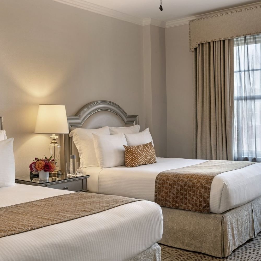 Two classic double beds with pillows and flowers in a room at Warwick Melrose in Dallas.