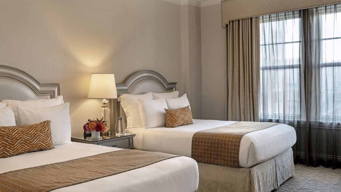 Two queen beds with geometric throws by a lamp under curtains in Classic Double at Warwick Melrose Dallas