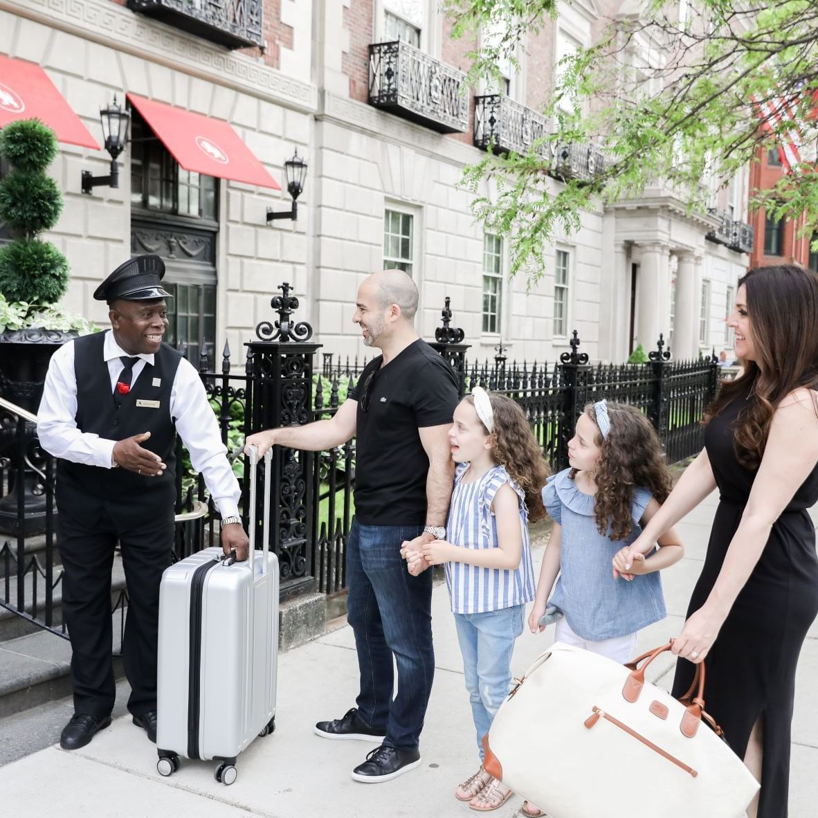 A bellman greeting a family of four in front of The Eliot Hotel
