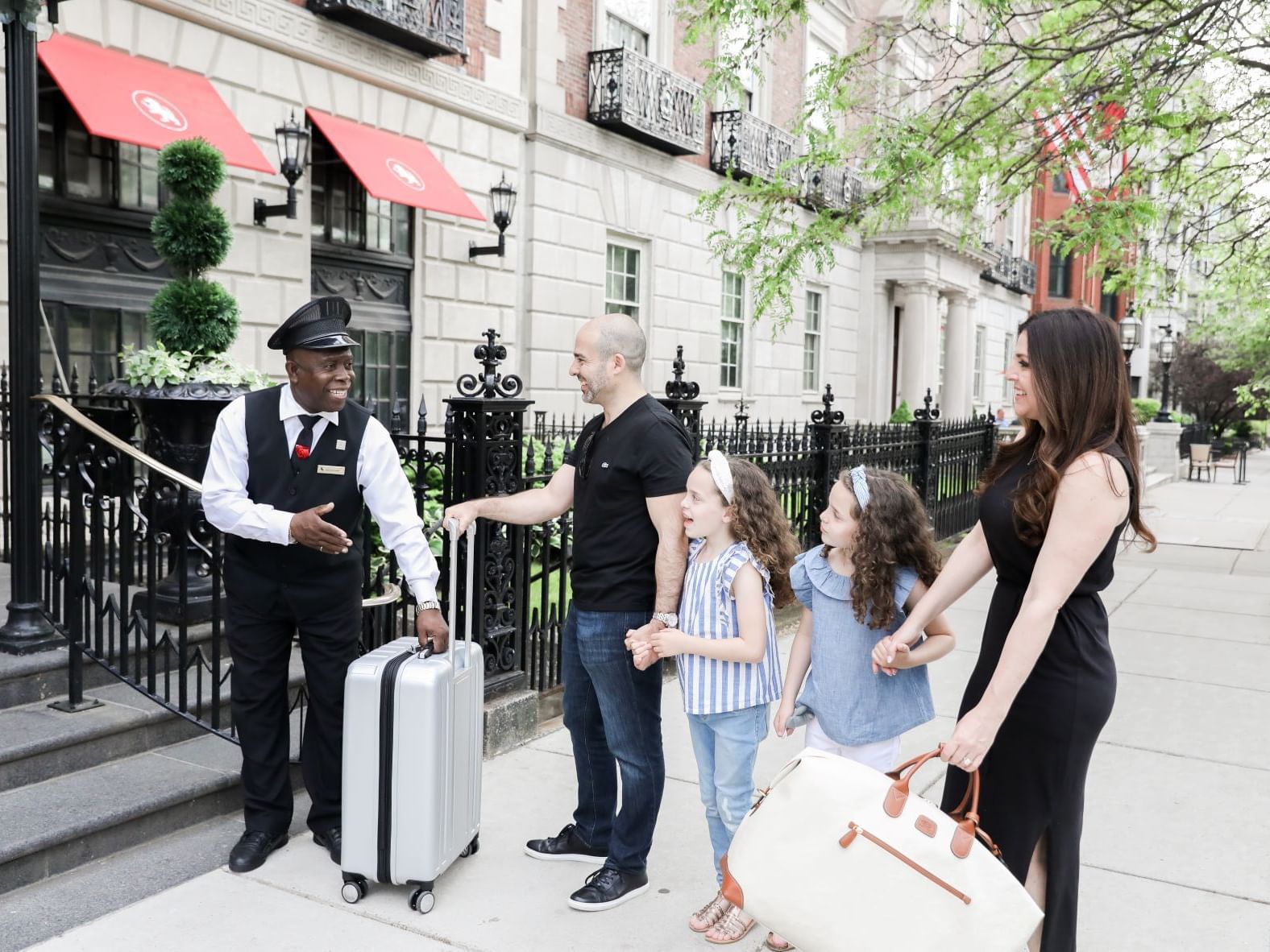 A family being greeted by a doorman and being brought into the hotel.