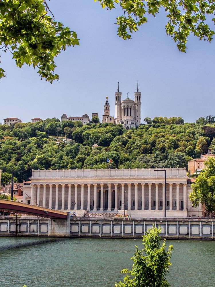 Lyon with white columns by a river, under a green hill with a cathedral near Warwick Hotels & Resort