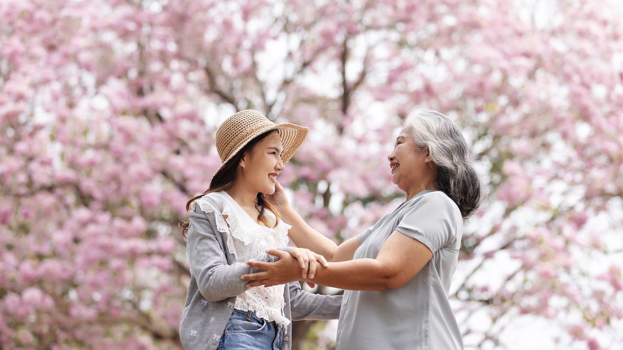 Woman and older woman smiling beneath blooming cherry blossoms