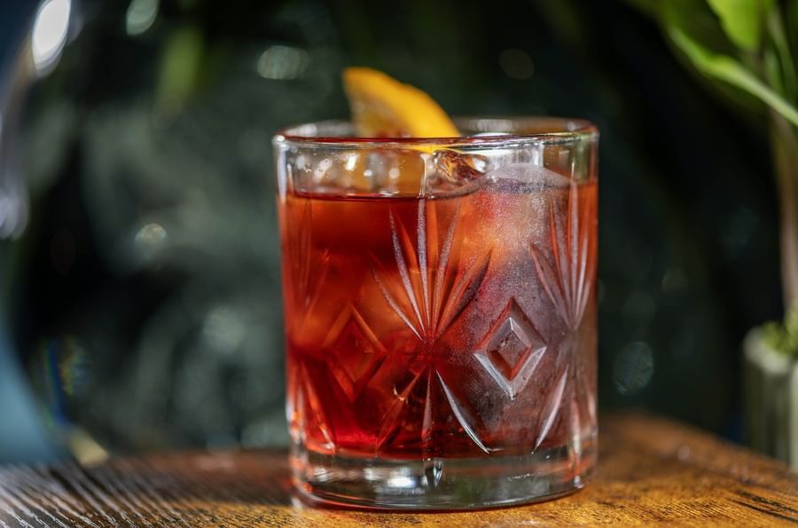 Close-up of a dark red cocktail with an orange slice on a wooden bar at The Capital Hotel, Apartments and Townhouse