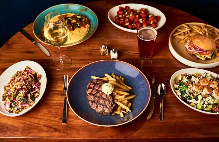 Multiple dishes and drinks including steak, salad, fries, burgers, and wine served at the Hotel Arista.
