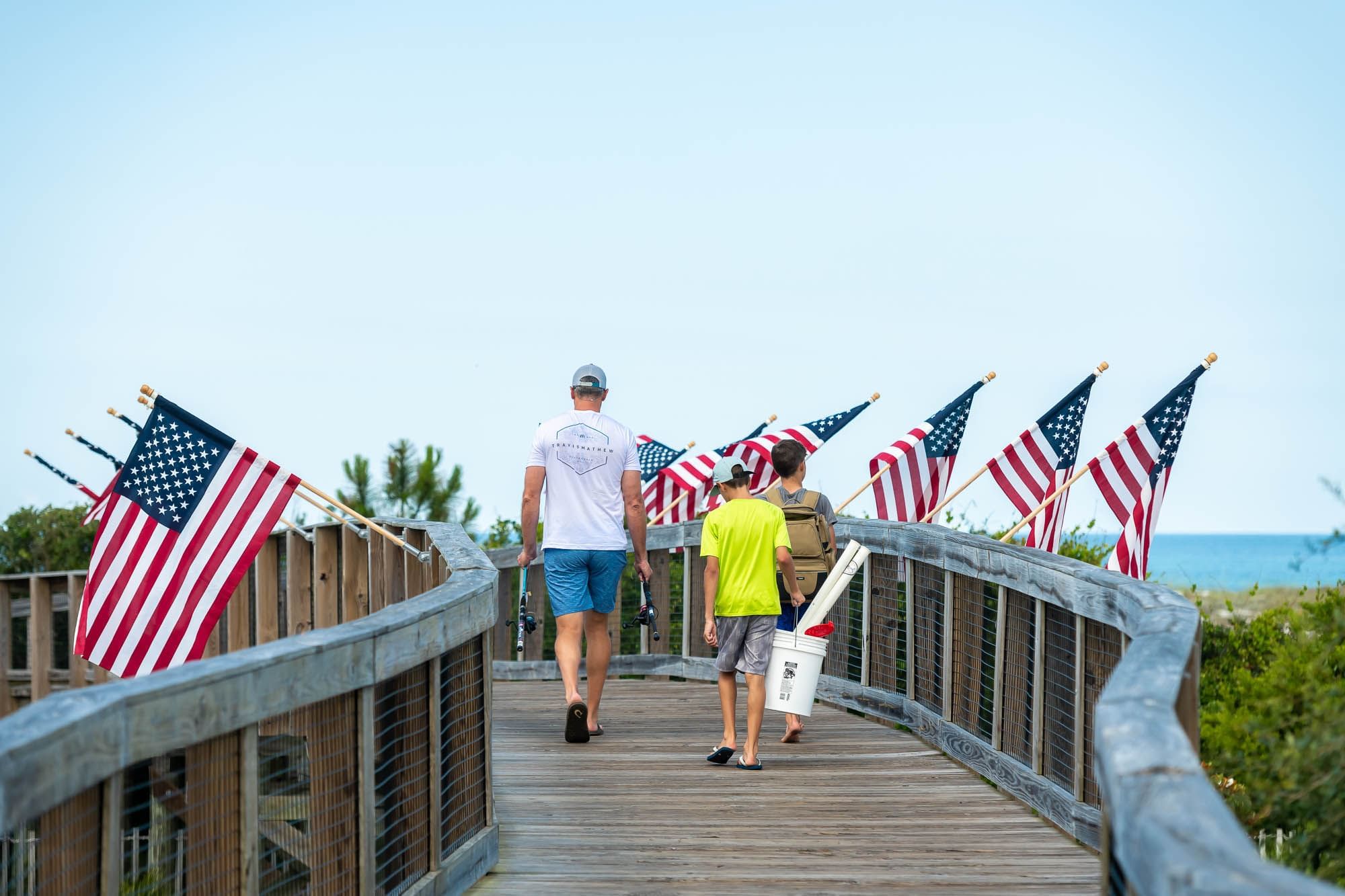 A family walks down the Watersound Beach Club boardwalk lined with American flags heading to the beach