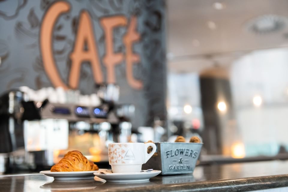 A cup of coffee served with a croissant served on the cafe counter at Hotel Vila Centric