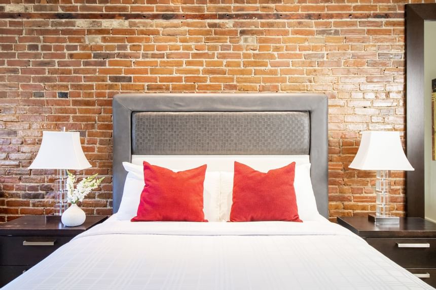 queen bed with two red accent pillows with exposed brick wall