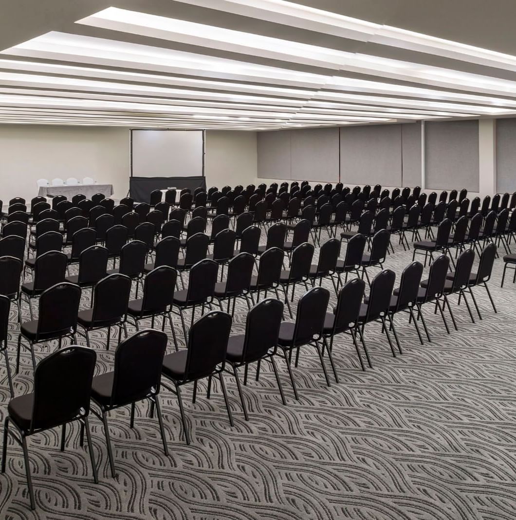 Large theater-style event space with rows of black chairs and dual projection screens at Real Inn Celaya