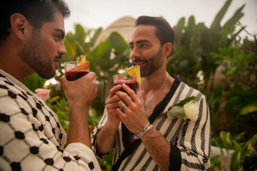 Two men enjoying tropical cocktails with pineapple garnish among lush greenery at Almar LGBT Luxury Resort