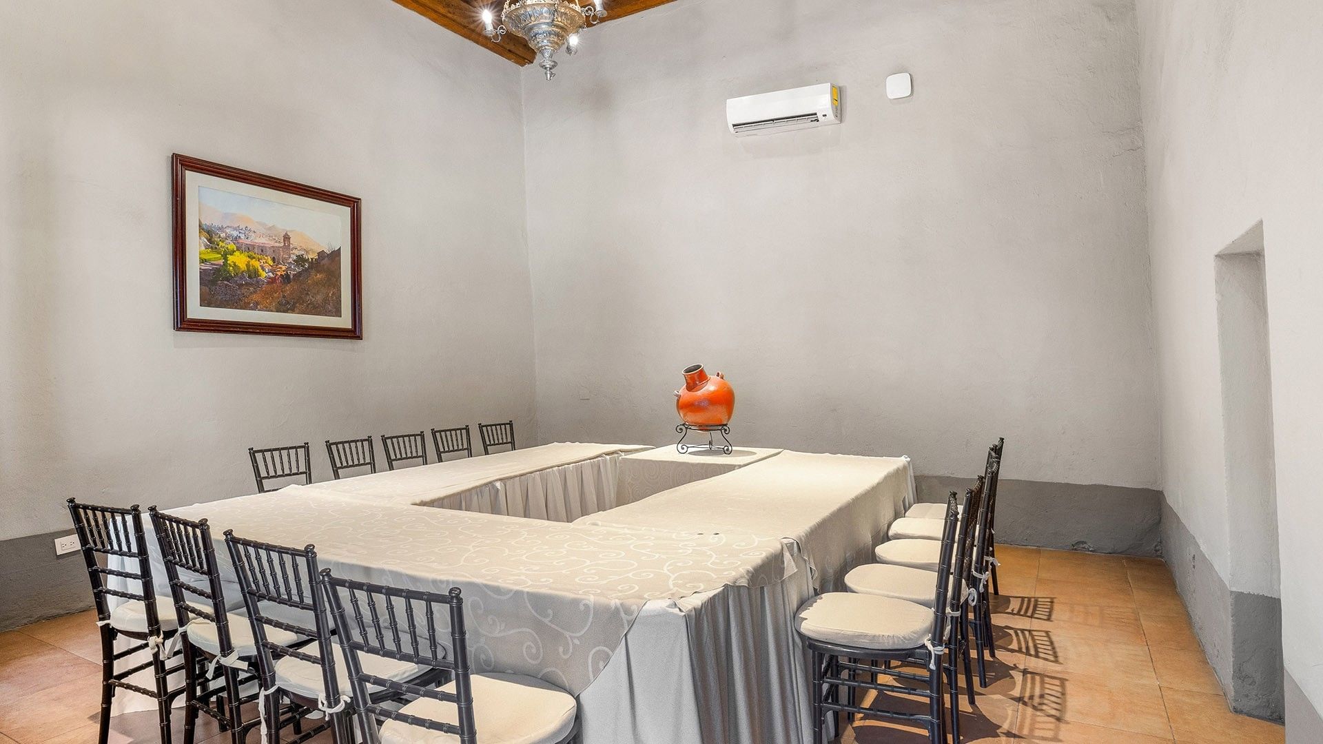 White U-shaped banquet table with black chairs and a red clay pot in a stone room at Quinta Real Puebla