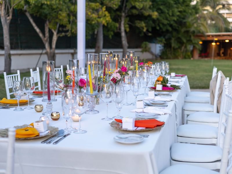 Long outdoor table with elegant decor and lit candles set in tropical surroundings at Fiesta Americana Riviera Nayarit Resort & Spa.
