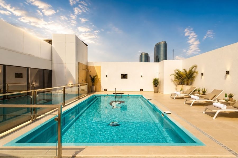 Rooftop swimming pool with dolphin mosaic tile under clear blue sky near loungers on terrace at Naviti by Warwick Jeddah