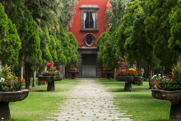 Cobblestone pathway leading to a Fiesta Americana Hacienda Galindo Resort & Spa flanked by green trees and flowerpots