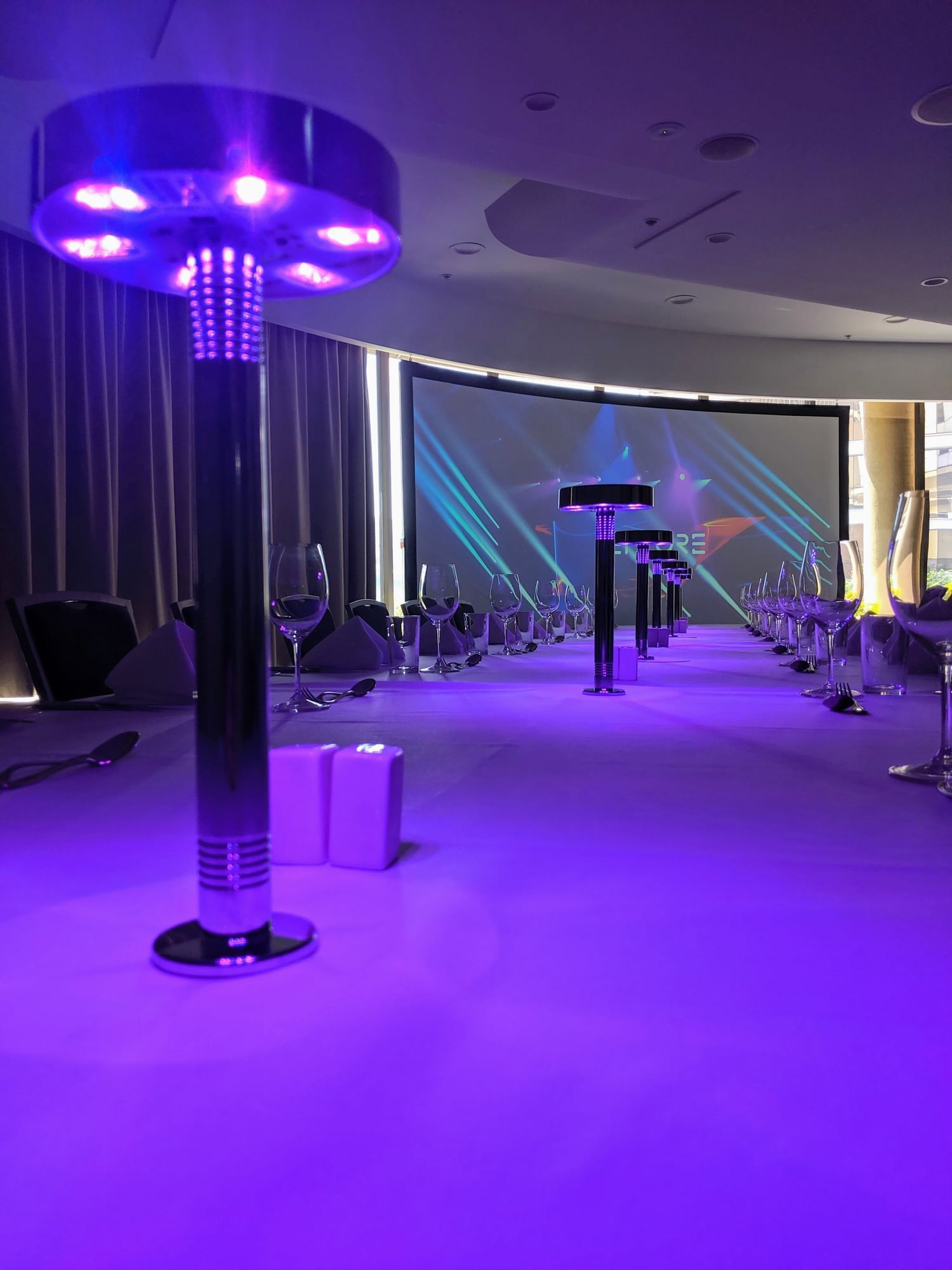 Conference table set with glowing purple lights and glassware facing a projection screen at Pullman Sydney Olympic Park