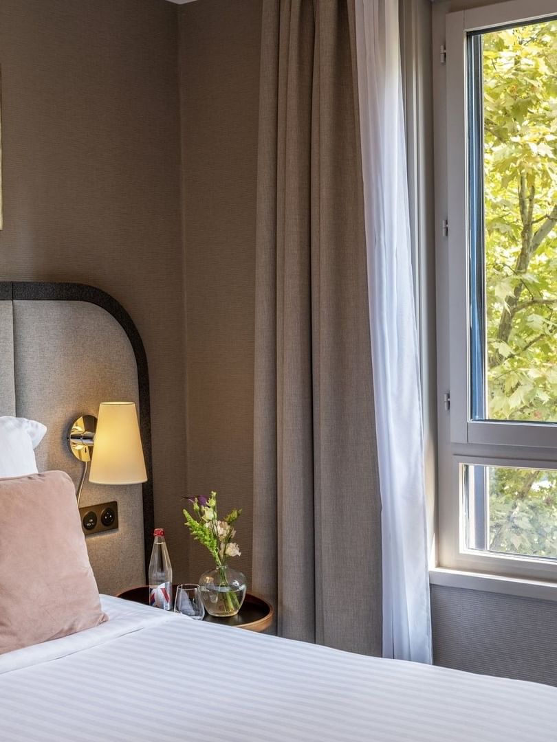 Nightstand by the bed with cushioned headboard & a lush greenery view in the Premium Suite at Warwick Reine Astrid - Lyon