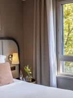Nightstand by the bed with cushioned headboard & a lush greenery view in the Premium Suite at Warwick Reine Astrid - Lyon