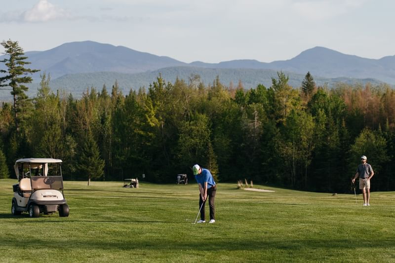 Golfer putting on scenic green course near golf cart with mountain view in background at Mountain View Grand Resort & Spa