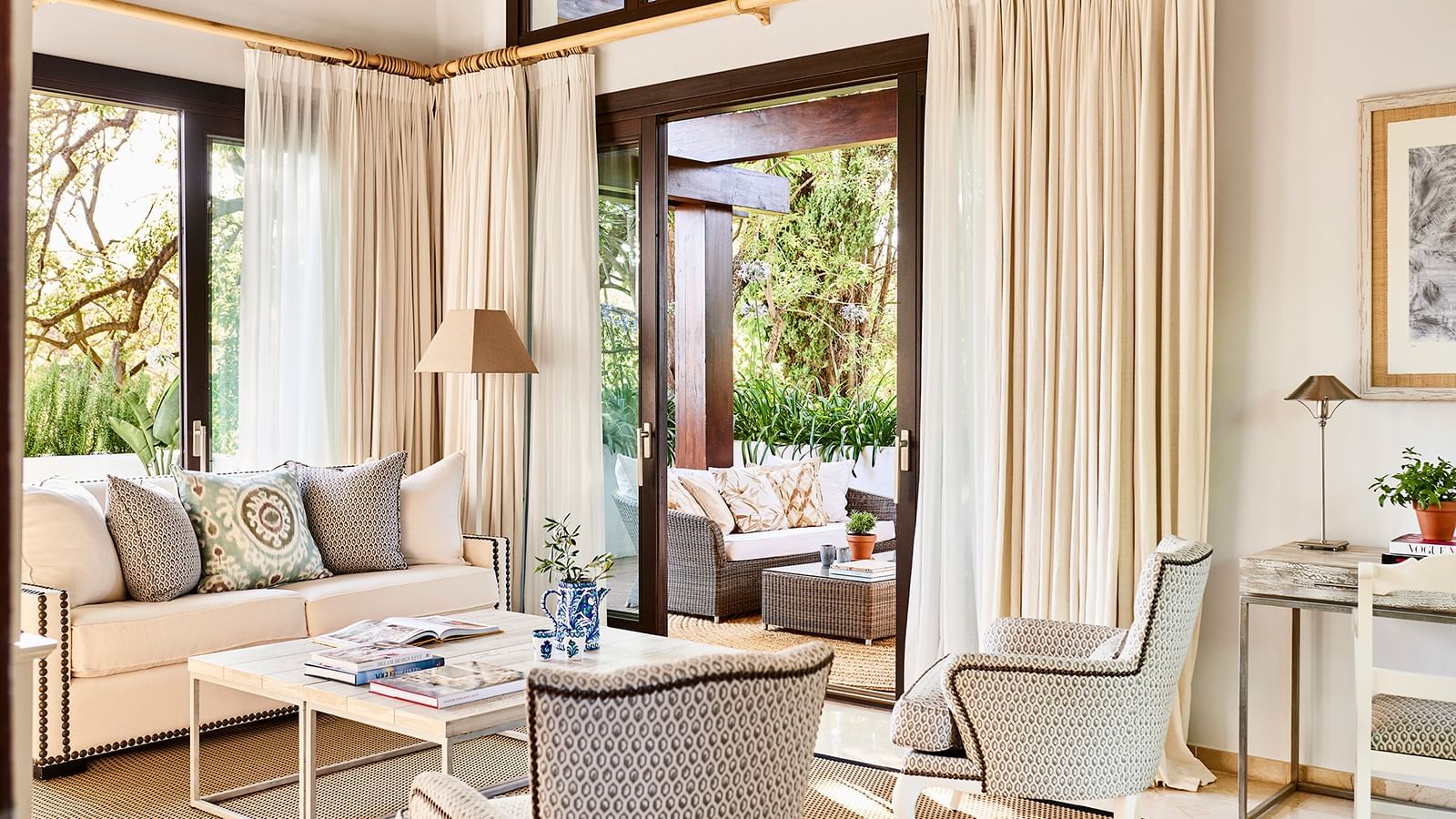Room with a chair and ottoman placed by sliding doors that open to a green balcony at the Marbella Club