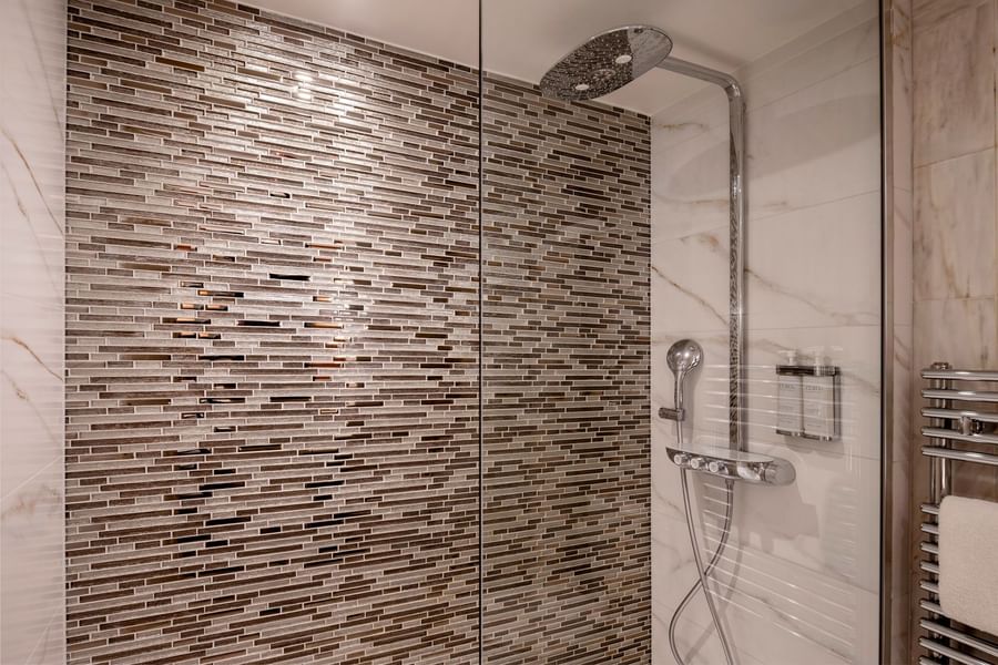 Modern bathroom with glass-enclosed shower featuring mosaic tile accent wall and rainfall showerhead at Warwick Brussels Grand-Place