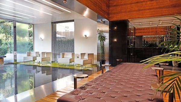 Tufted leather bench by metal tables near white armchairs under a wood ceiling at Warwick Stone 55 - Beirut