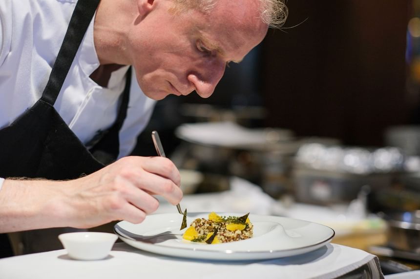 Chef carefully garnishing a plated dish, featuring grains and vibrant ingredients, in Square One at Park Hyatt Saigon