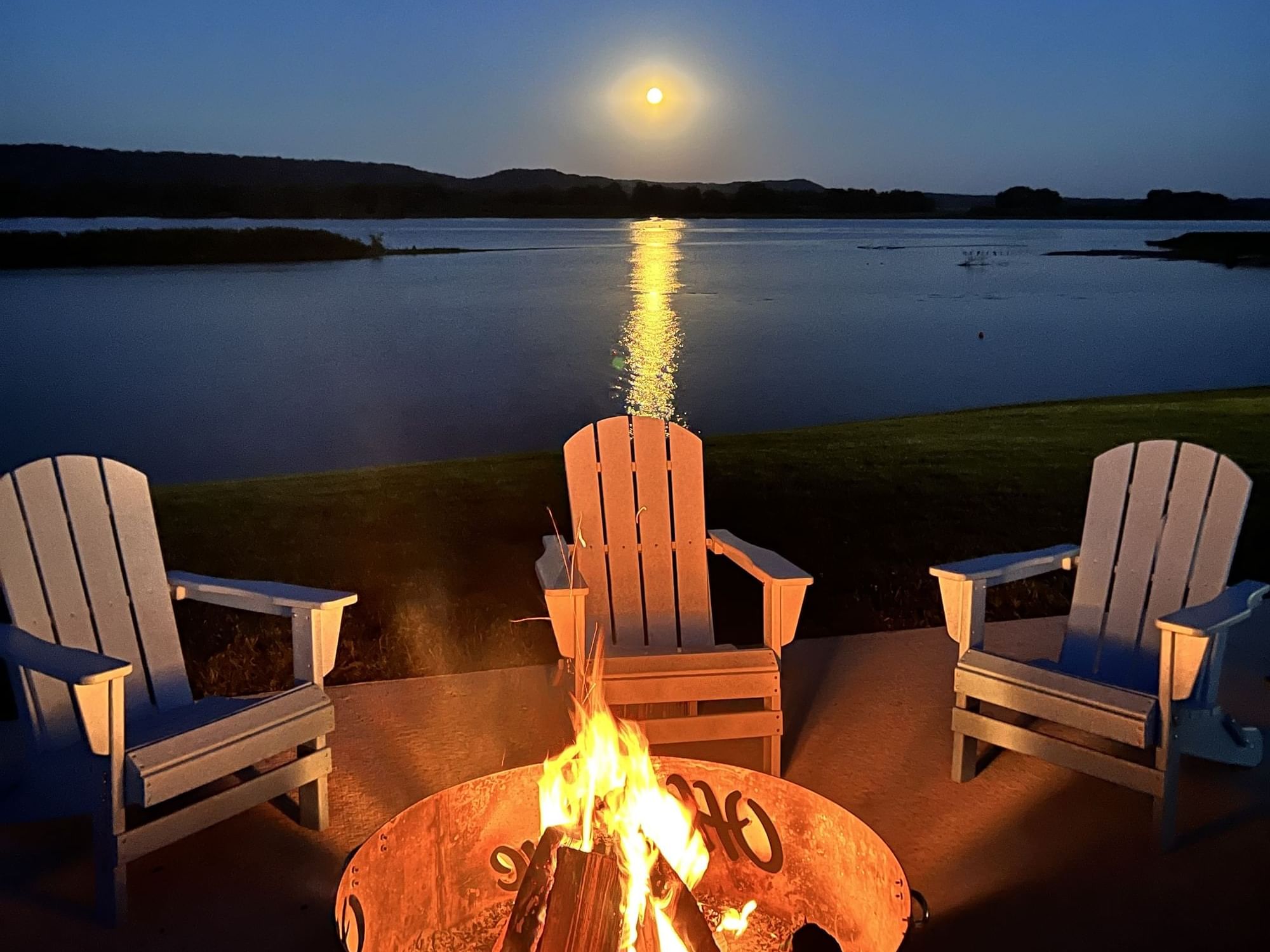 Mississippi riverside with a glowing campfire and four Adirondack chairs at the Riverfront Site in Off Shore Resort