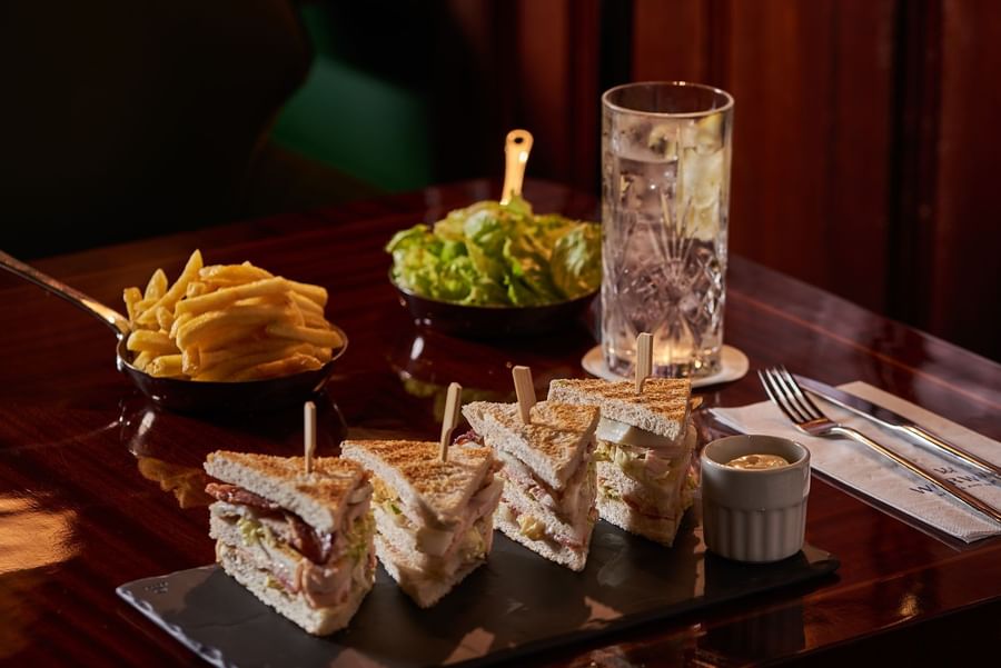 Club sandwiches with fries and salad by a glass of water on a dark wooden table at Hotel Westminster Paris