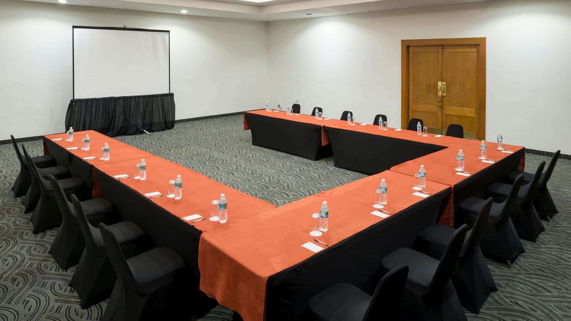 U-shaped table setup facing a projector screen by the door and carpet floors in Budapest at Real Inn Mexicali
