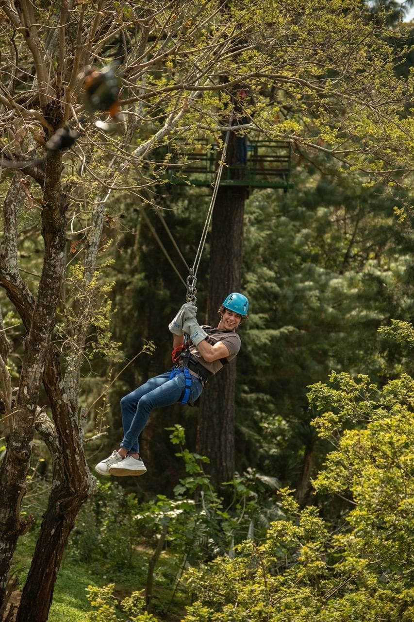 Persona feliz en canopy atravesando un frondoso bosque verde, con casco y arnés en Casa Santo Domingo