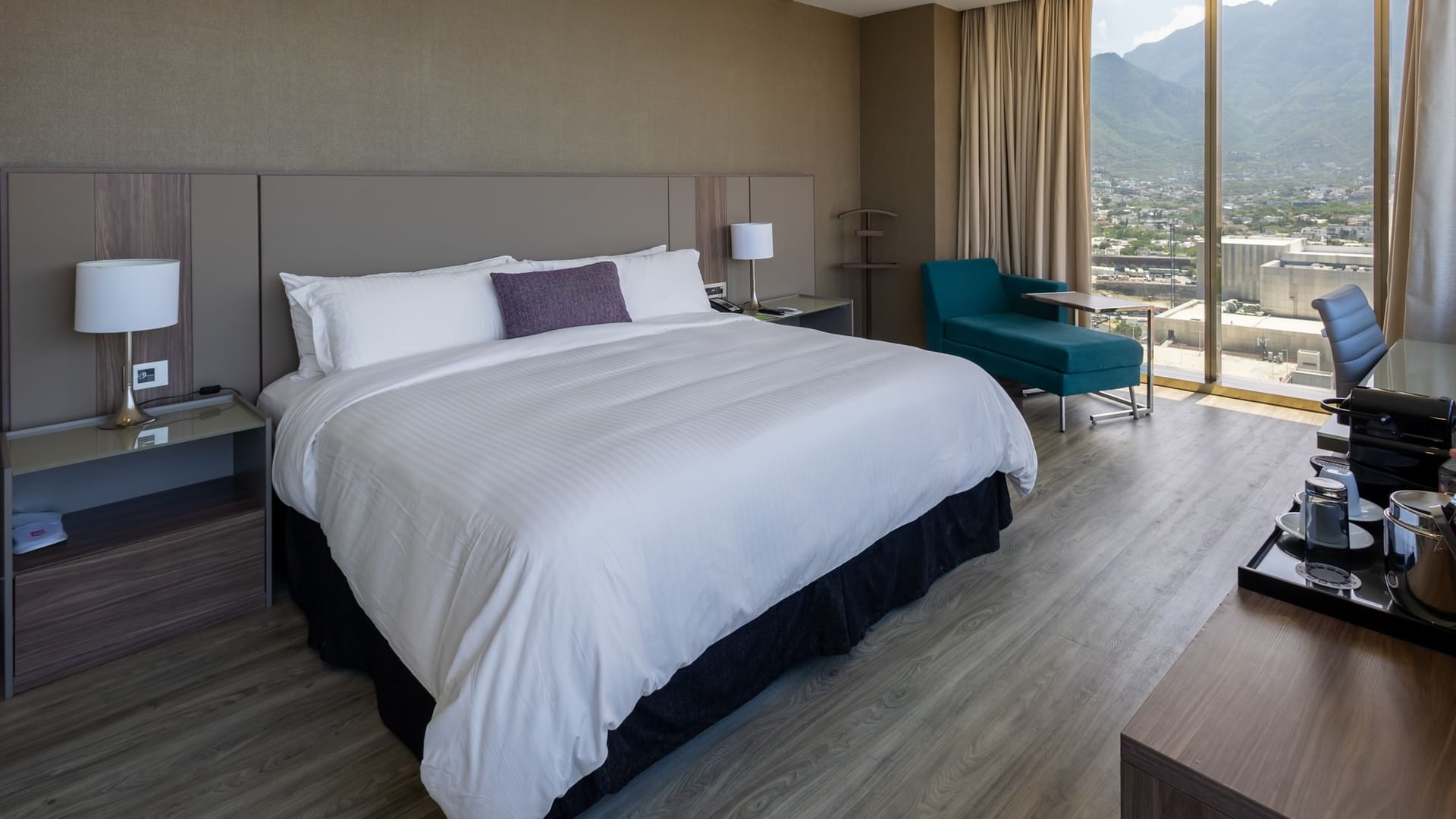 Junior Suite King con cama king, sillones turquesa y vistas a la montaña en Camino Real Fashion Drive Monterrey.