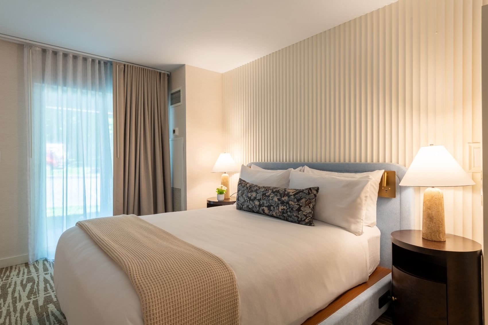 A hotel room with a bed, nightstand, and window
