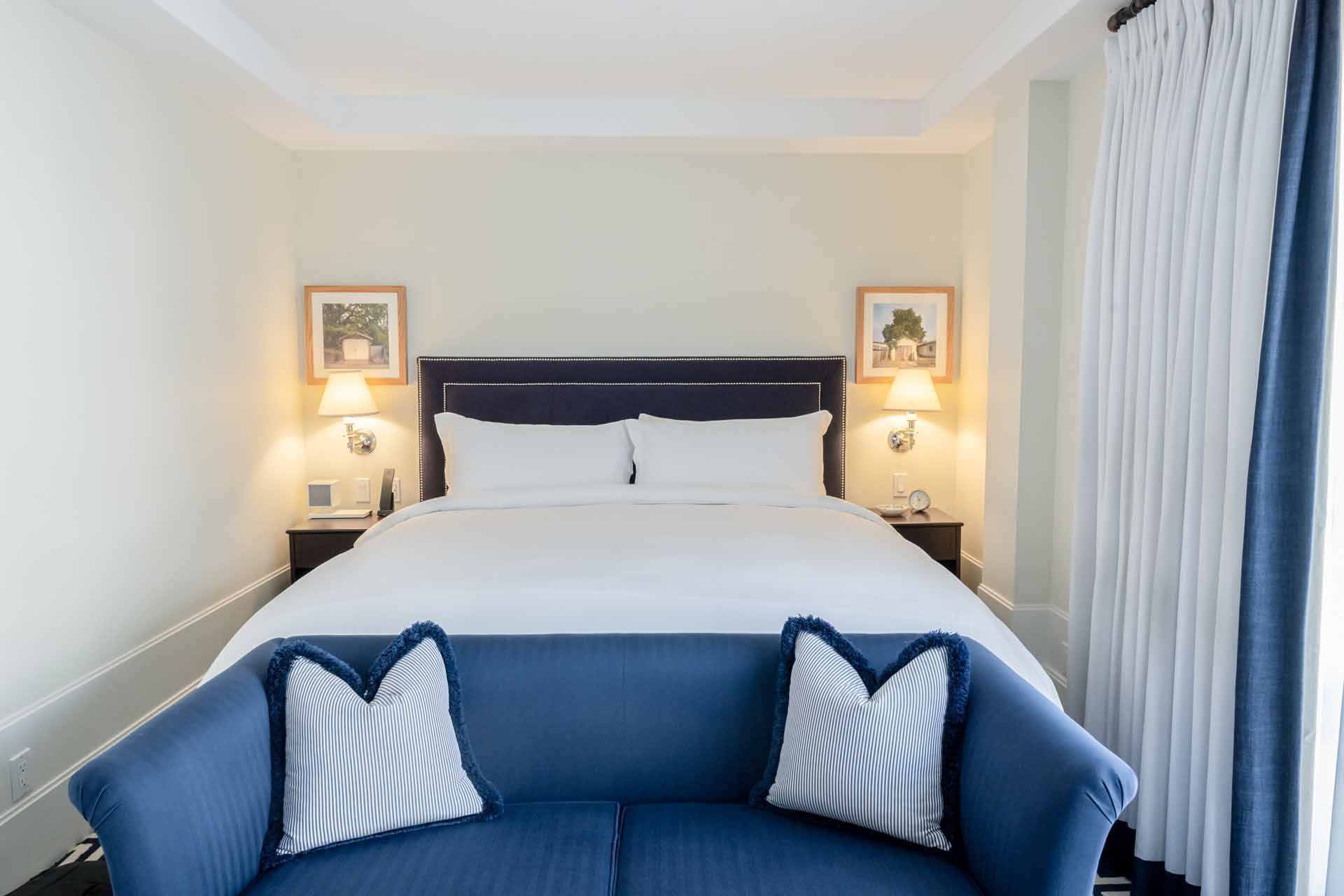 Well-appointed room with a comfy bed, blue couch, and hanging artwork at El Prado Hotel