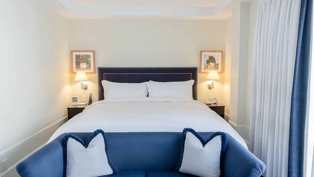 Deluxe Junior King Suite at El Prado Hotel featuring a cozy bed, a comfortable seating area, and two bedside lamps