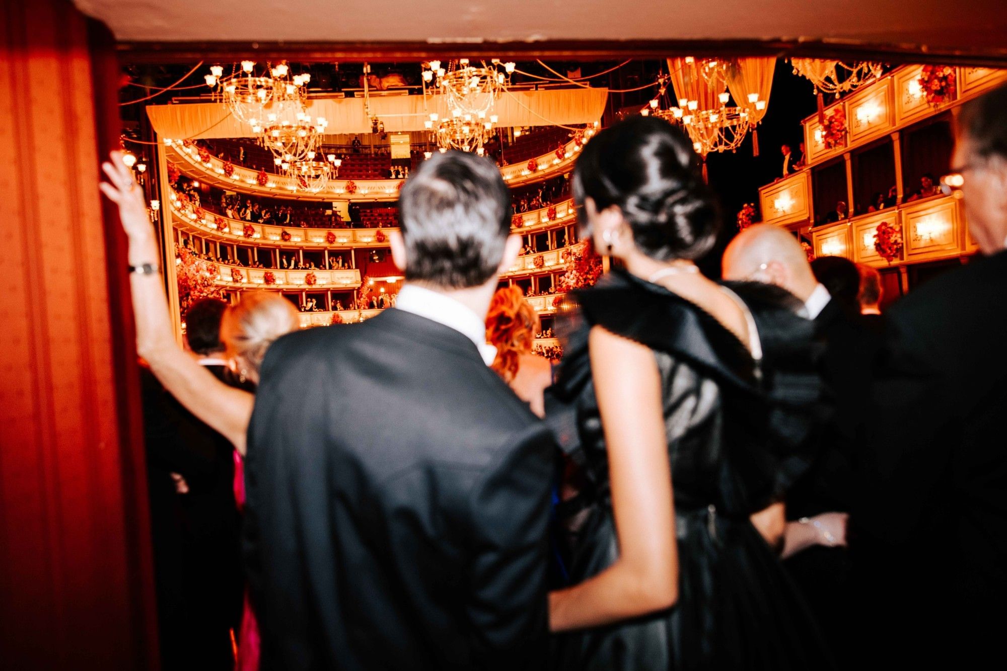 Elegantly dressed guests at the Vienna State Opera with a view of the illuminated auditorium and opera boxes