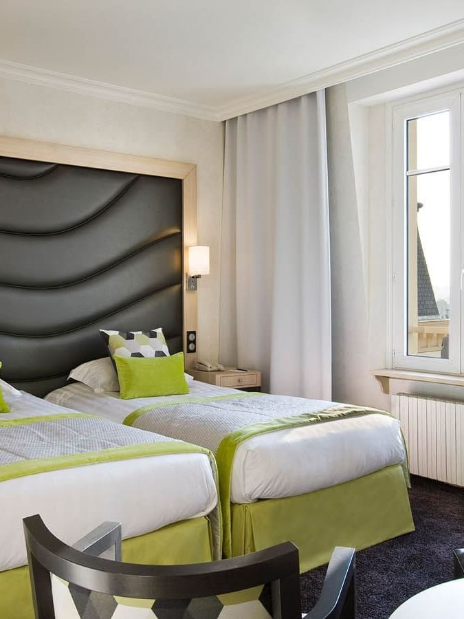 Two beds facing small seating area with a cushioned headboard in Escale Supérieure at Le Grand Hôtel des Thermes