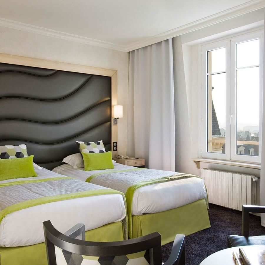Two beds facing small seating area with a cushioned headboard in Escale Supérieure at Le Grand Hôtel des Thermes