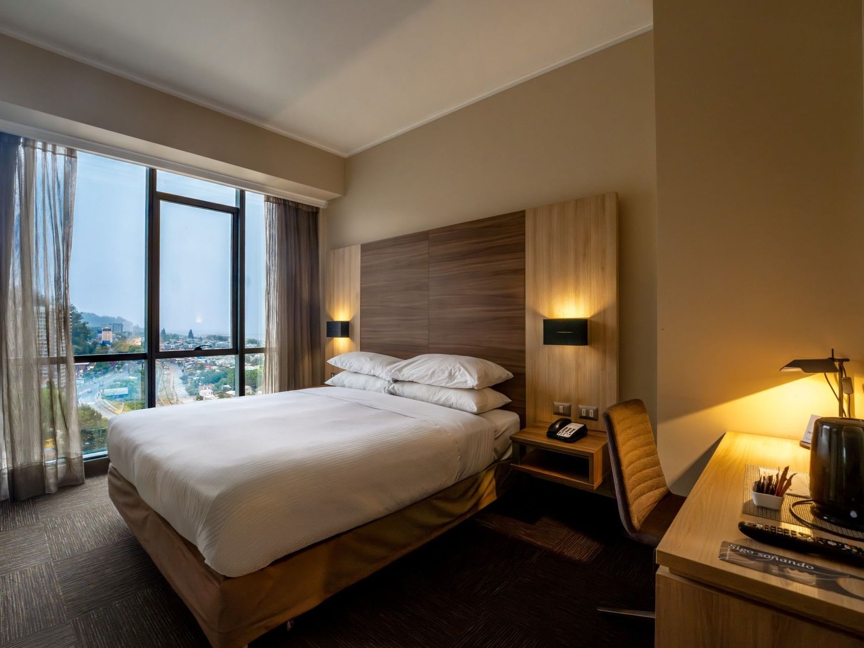 Habitación de hotel con cama, escritorio, silla y ventana en el hotel HCC Costanera Concepción.