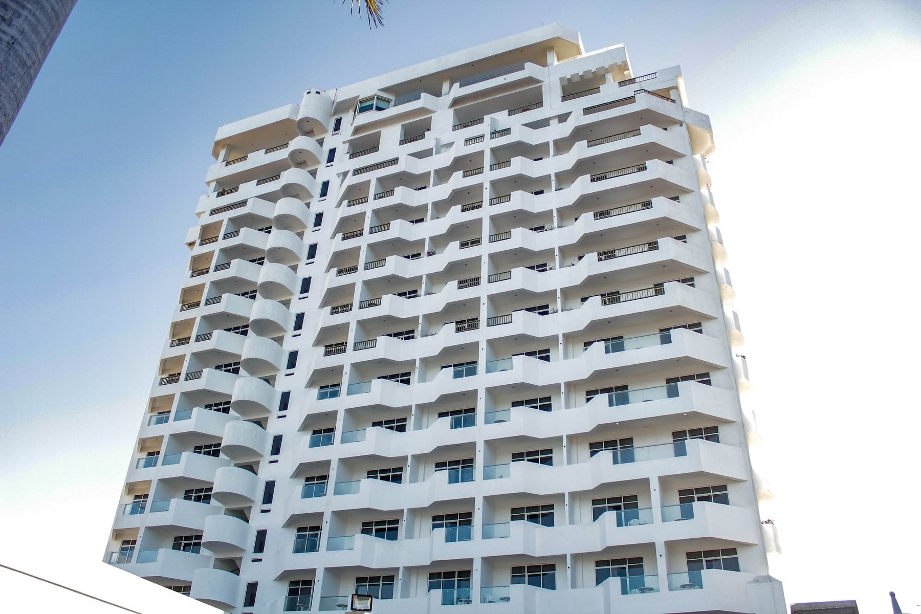 The white Sunvivia Mazatlán resort building exterior with palm trees and a paved entrance under a blue sky