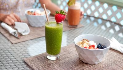Tall green smoothie glass with a strawberry garnish beside a fruit and yogurt breakfast bowl at Worthing Court Apartment