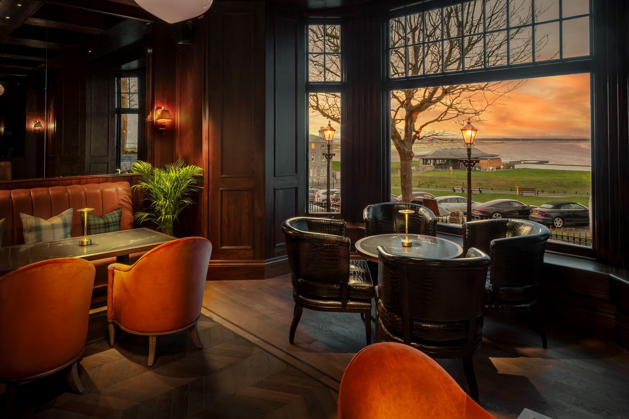 Bow Butts Bar, featuring brown leather chairs, a cozy table, and sunset views through wide windows at Seaton House