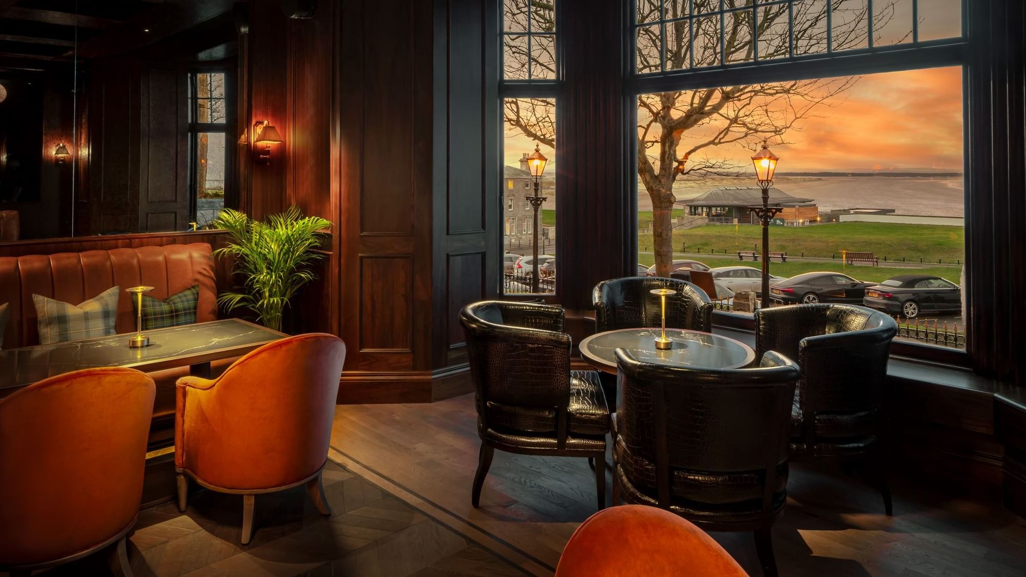 Bow Butts Bar, featuring brown leather chairs, a cozy table, and sunset views through wide windows at Seaton House