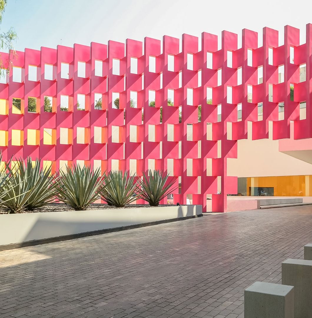 Muro rosa vibrante con celosía junto a plantas de agave en maceta gris bajo un cielo despejado en Camino Real Polanco México