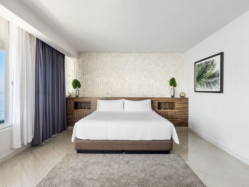 Penthouse Luxury bedroom with a white king-size bed, textured stone wall, and palm tree wall art at Sunvivia Mazatlán