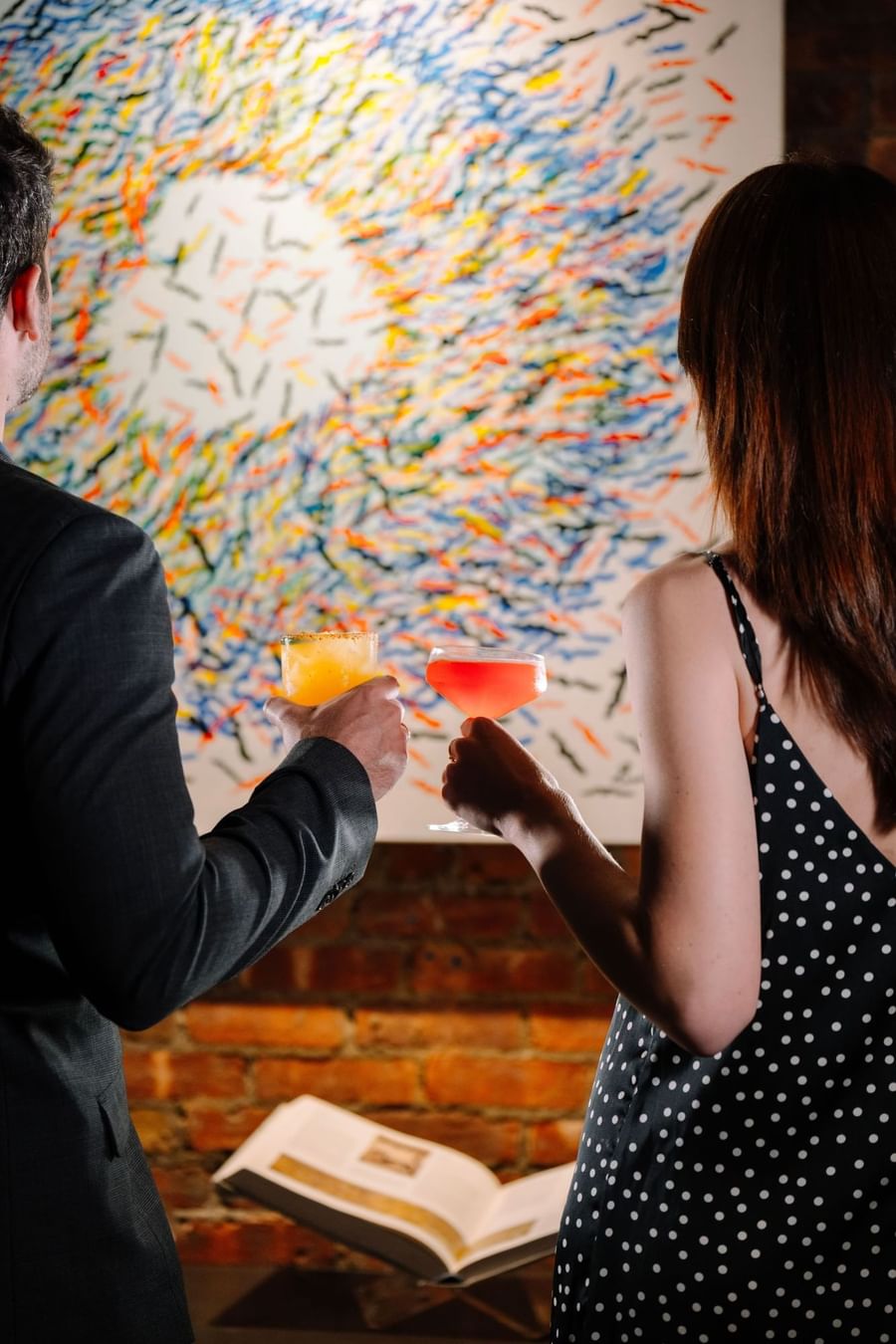 A man and a woman holding drinks in the lobby of the Art House Hotel NYC, in front of an abstract painting.