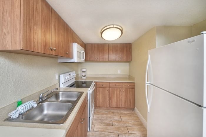 A small kitchen with wood cabinets, a sink, stove, microwave, and refrigerator.