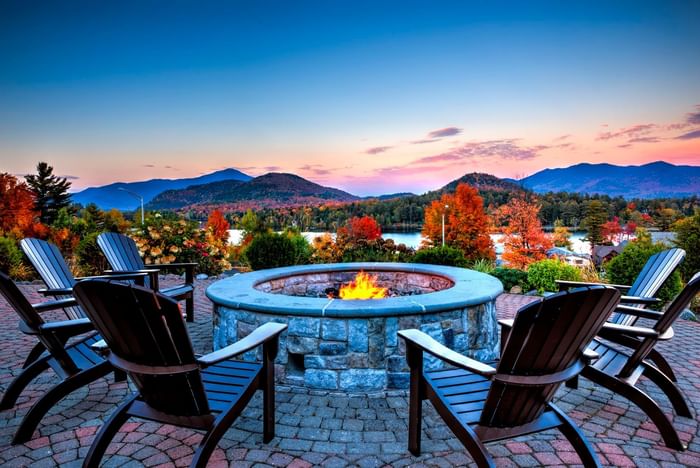 Adirondack chairs surround a stone fire pit on a patio at Lake Placid Club Grandview overlooking the colorful mountains