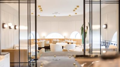 Elegant restaurant interior with arched windows, white furniture, and decorative lighting fixtures.