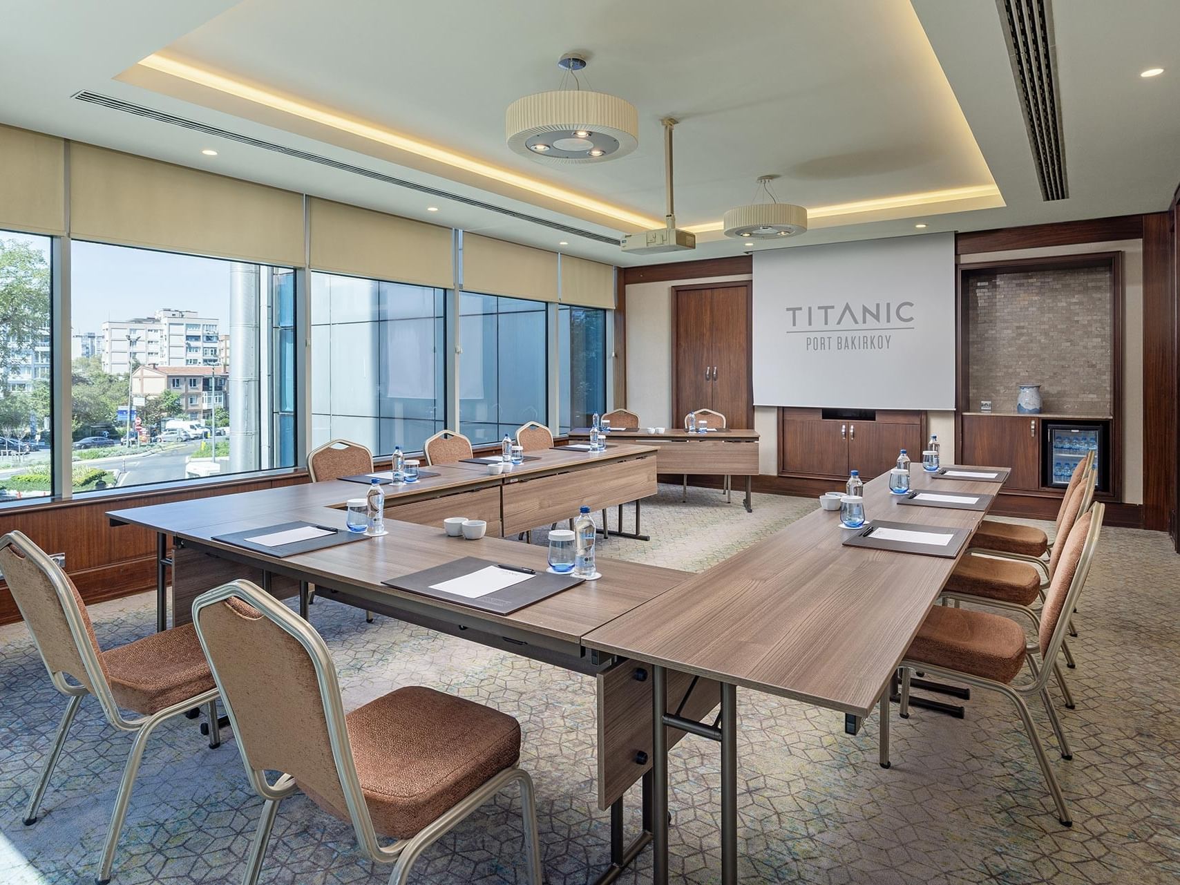 Aegean toplantı salonunda projeksiyon perdesiyle U şeklinde masa kurulumu ve şehir manzaralı geniş pencereler Titanic Port Bakırköy’de.